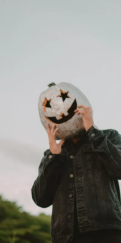 Persona con una calabaza tallada tipo Jack-O'-Lantern cubriéndole la cabeza a modo de máscara, con cazadora vaquera negra