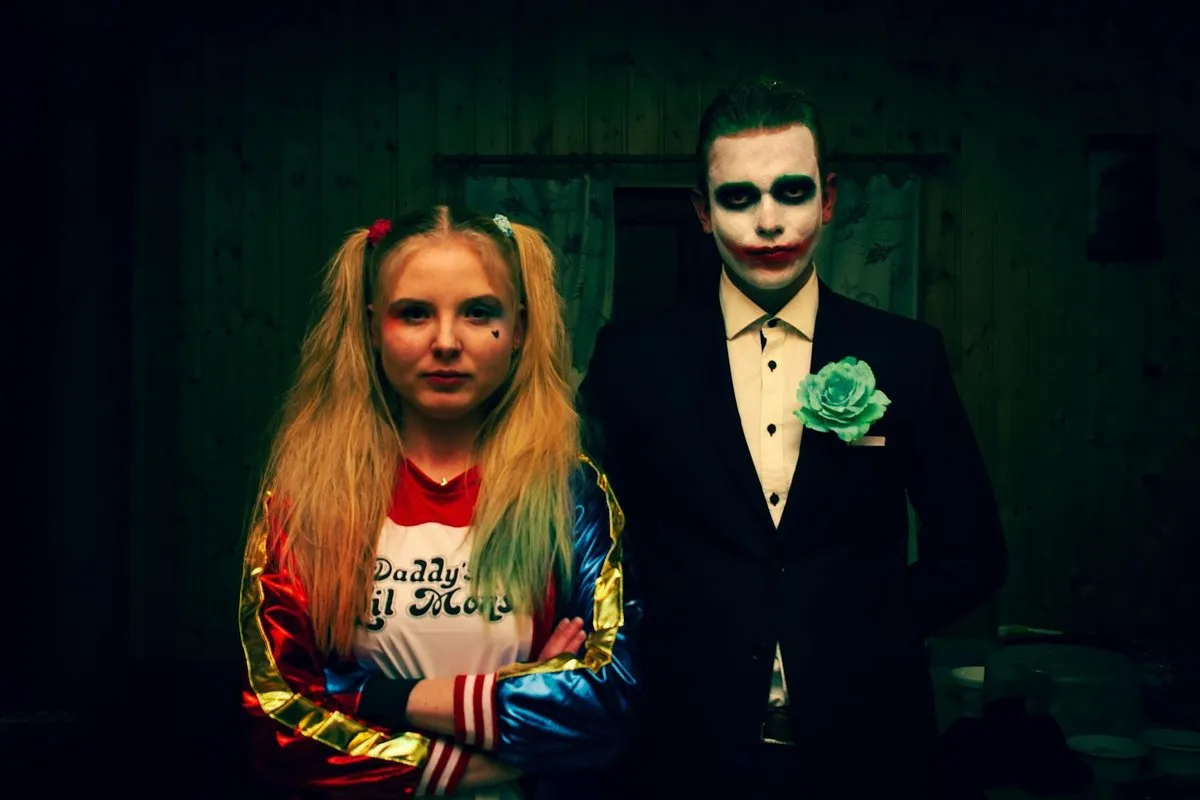 Pareja disfrazada de Joker y Harley Quinn, él con traje negro, cara pintada de blanco y labios rojos, ella con chaqueta bicolor y coletas rubias con puntas de color