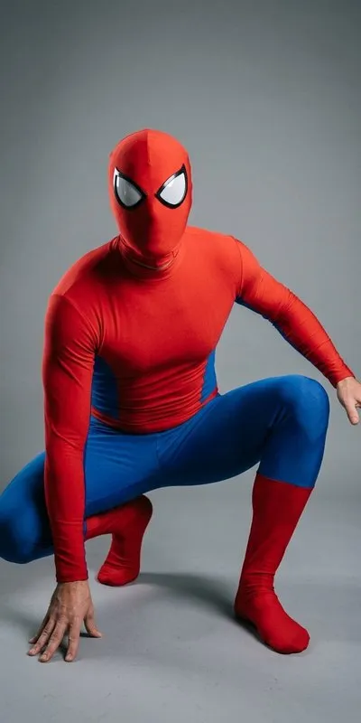Persona adulta con mono integral liso rojo y azul de superhéroe, sin dibujos ni logotipo, y máscara integral roja con ojos blancos, en pose agachada